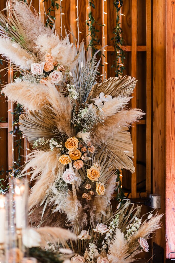 Close-up of boho floral installation with pampas grass, roses, and greenery on a wooden backdrop inside The Paseo.