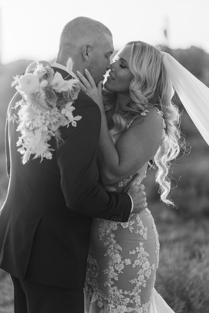 Black and white photo of bride and groom in a romantic kiss with desert sunlight highlighting her veil