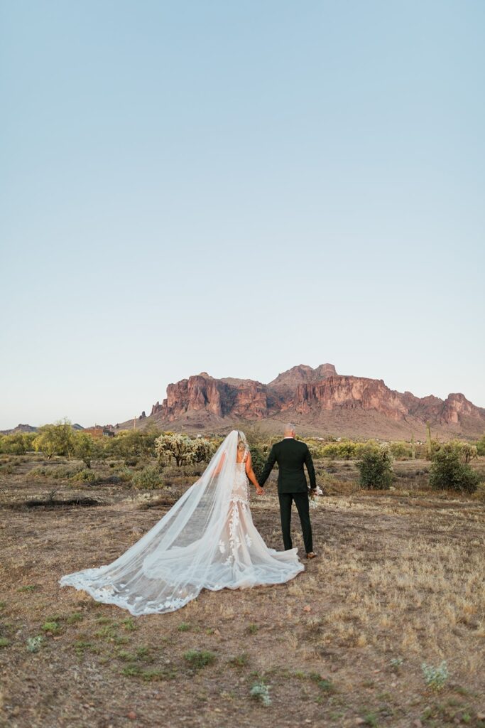 Bride and groom walking hand in hand toward the Superstition Mountains at The Paseo wedding venue in Arizona.